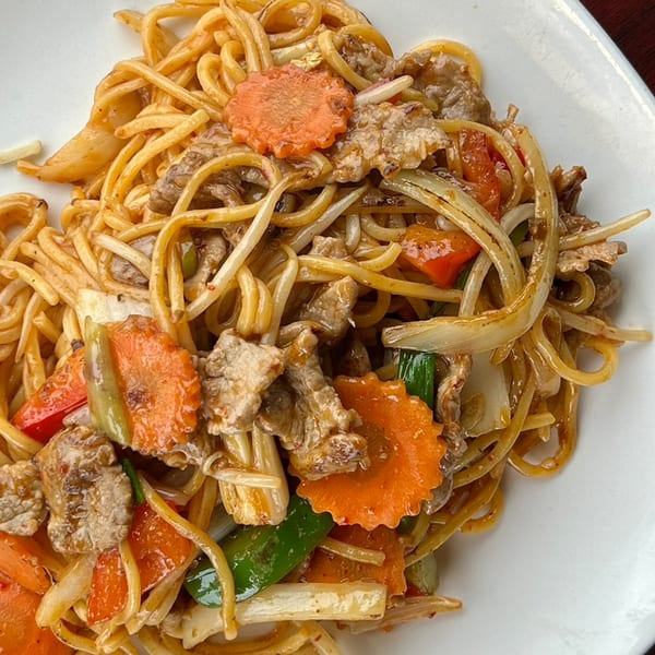 Close-up of Bangkok Bistro's Thai noodles with beef, carrots, and mixed vegetables on a white plate.