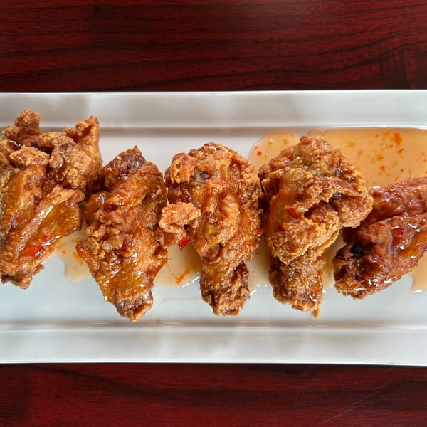 Five crispy fried chicken wings with sweet chili sauce on a white rectangular plate.