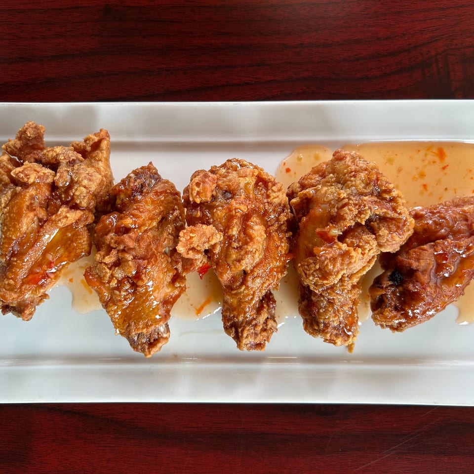 Five crispy fried chicken wings with sweet chili sauce on a white rectangular plate.