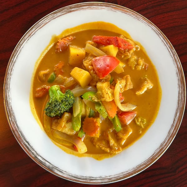 Close-up of a vibrant Thai curry with broccoli, red peppers, and other vegetables in a white bowl.