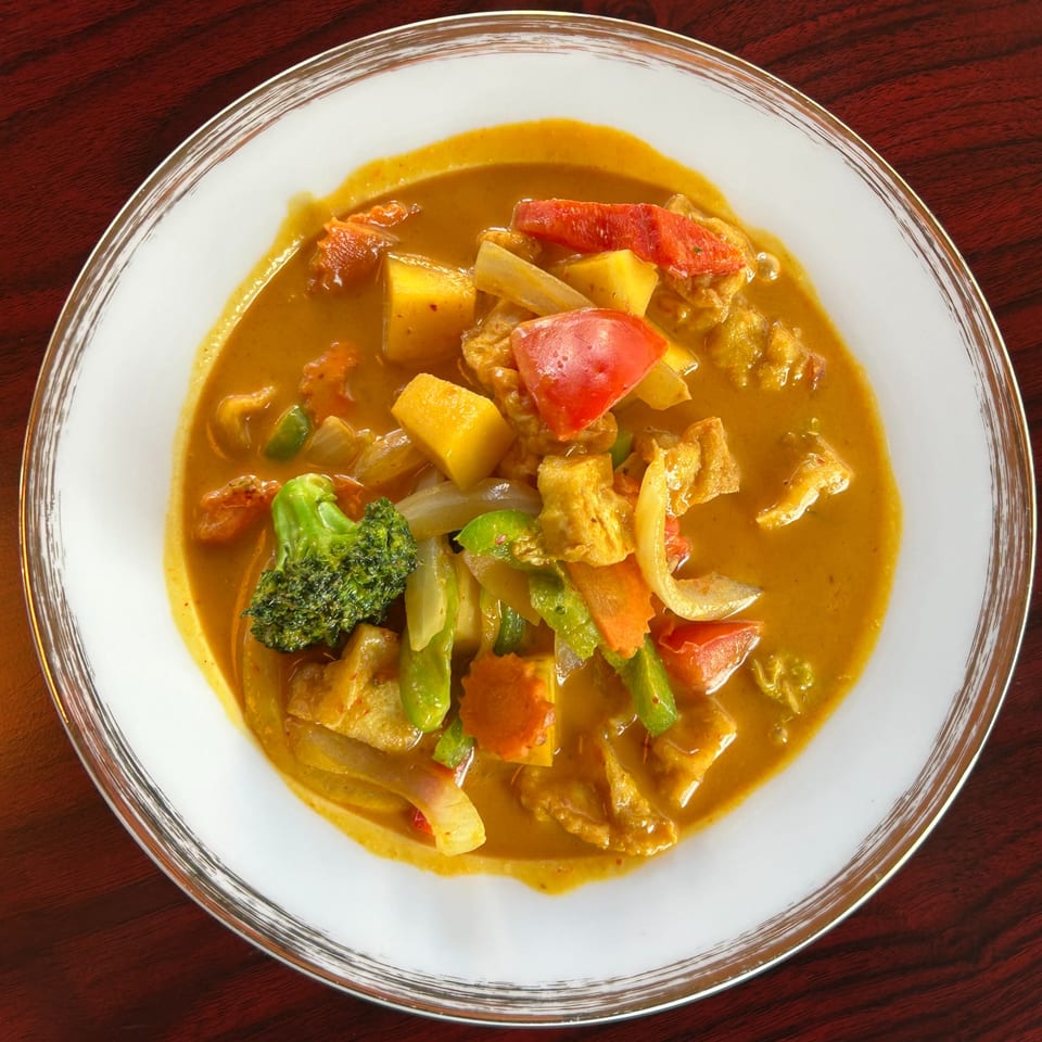 Close-up of a vibrant Thai curry with broccoli, red peppers, and other vegetables in a white bowl.