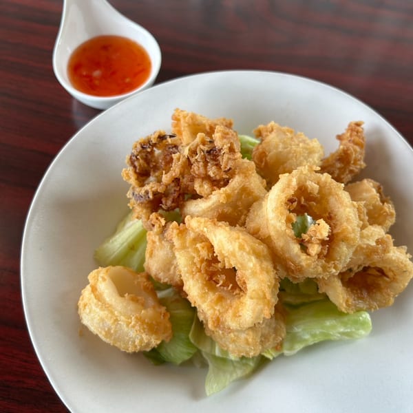 Crispy fried calamari rings and tentacles on lettuce, with a side of sweet chili sauce.