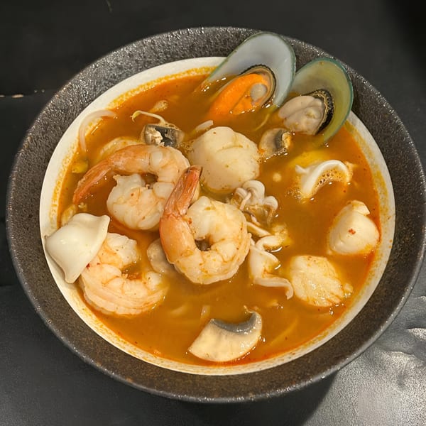 Close-up of a vibrant Thai Tom Yum soup with shrimp, mussels, scallops, and squid in a dark bowl.