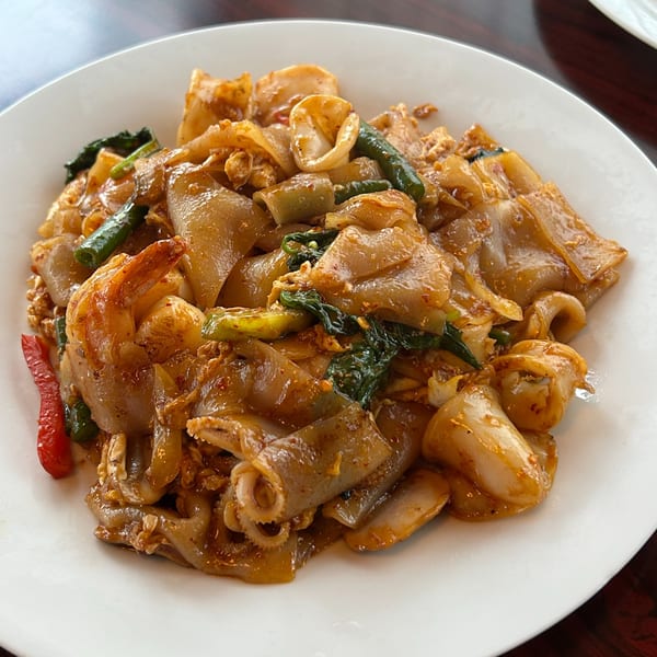 A plate of Bangkok Bistro's Pad Kee Mao with wide noodles, shrimp, squid, green beans, and red peppers.