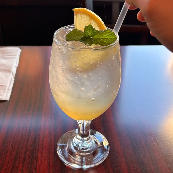 A refreshing Bangkok Bistro Thai Eatery drink with lemon, mint, and a straw on a wooden table.