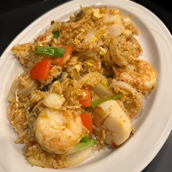 Thai seafood fried rice with shrimp, scallops, onions, red peppers, and green beans on a white plate.