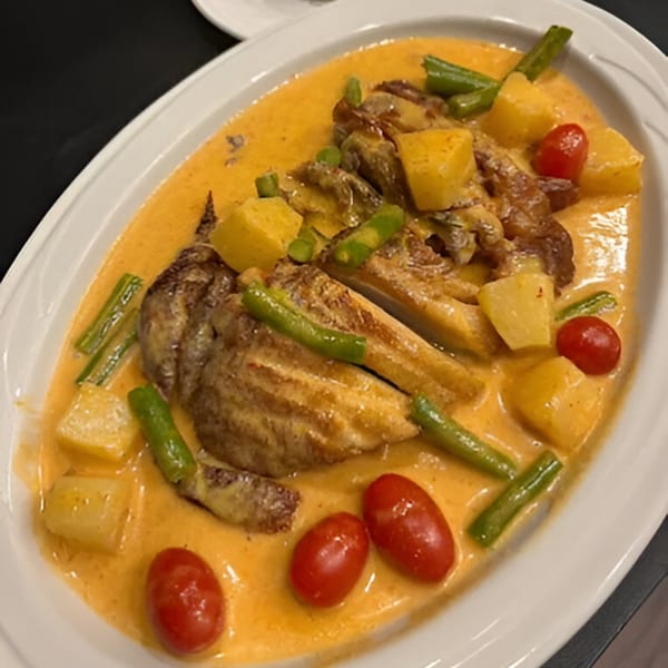 Thai red curry with roasted duck, pineapple, green beans, and cherry tomatoes on a white platter.