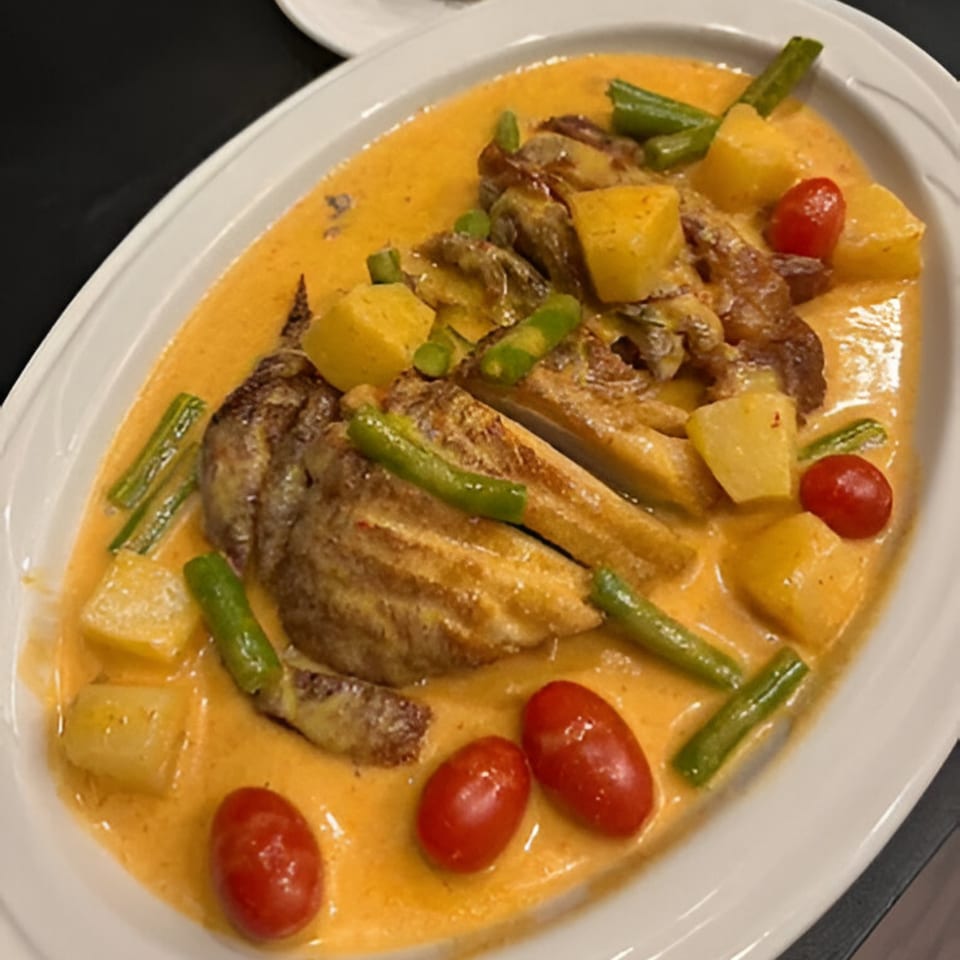 Thai red curry with roasted duck, pineapple, green beans, and cherry tomatoes on a white platter.