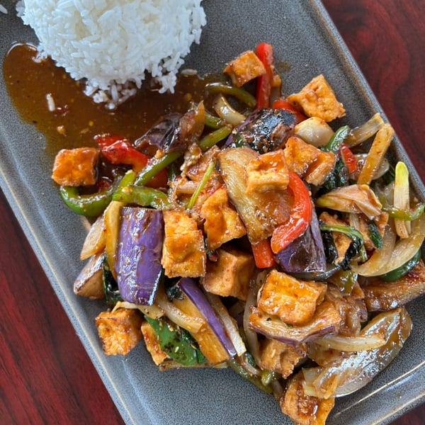 Thai stir-fried tofu, eggplant, bell peppers, and onions with white rice on a gray plate.
