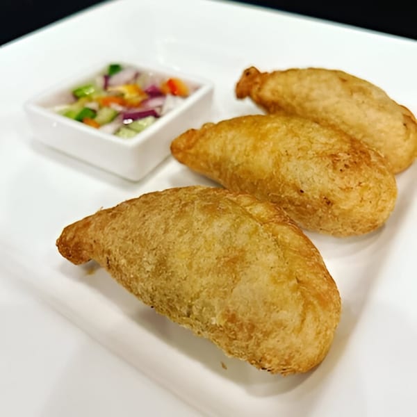 Three golden-brown Thai curry puffs with a side of colorful dipping sauce on a white plate.